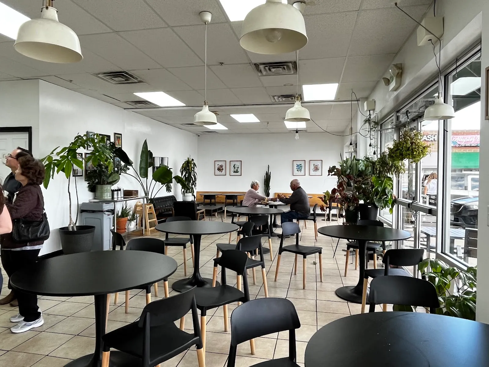 Bright dining room at Vinh Xuong Bakery with black tables, big windows, and plants
