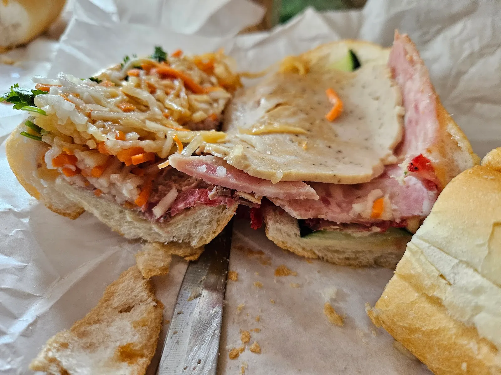 Banh mi cut in half, layered with meats, pate, pickled carrots, and cilantro